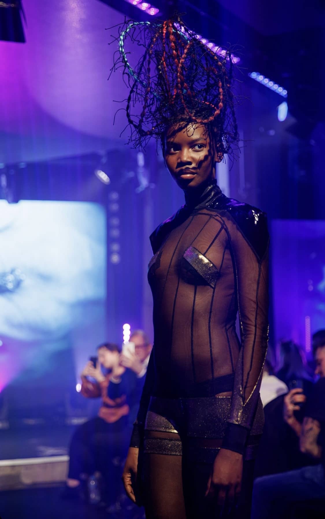Woman in mesh-clothes with hair suspended upwards at a fashion show, different angle
